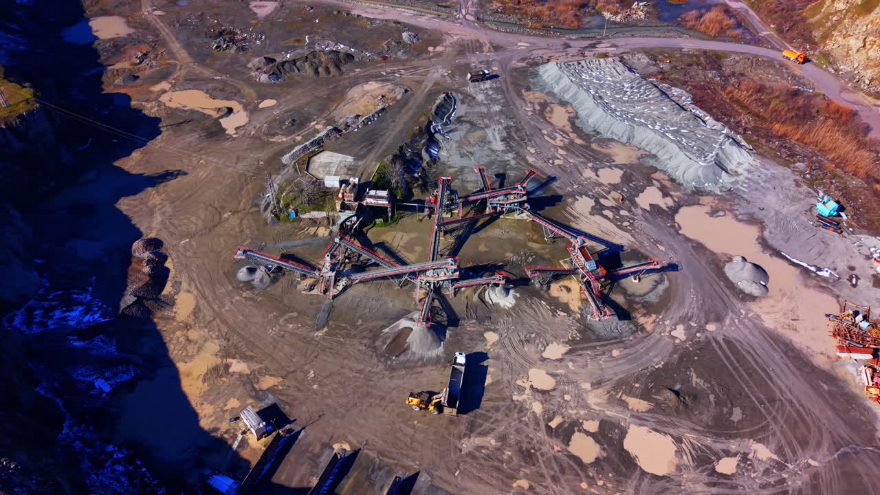 Complex network of conveyor belts and crushing machinery in a stone quarry with piles of processed gravel and trucks. Aerial view of stone processing conveyor belts and equipment