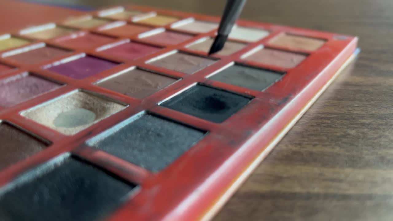 un pincel se sumerge en un color de una paleta de colores y recoge algo de color - primer plano de una paleta de colores en una mesa