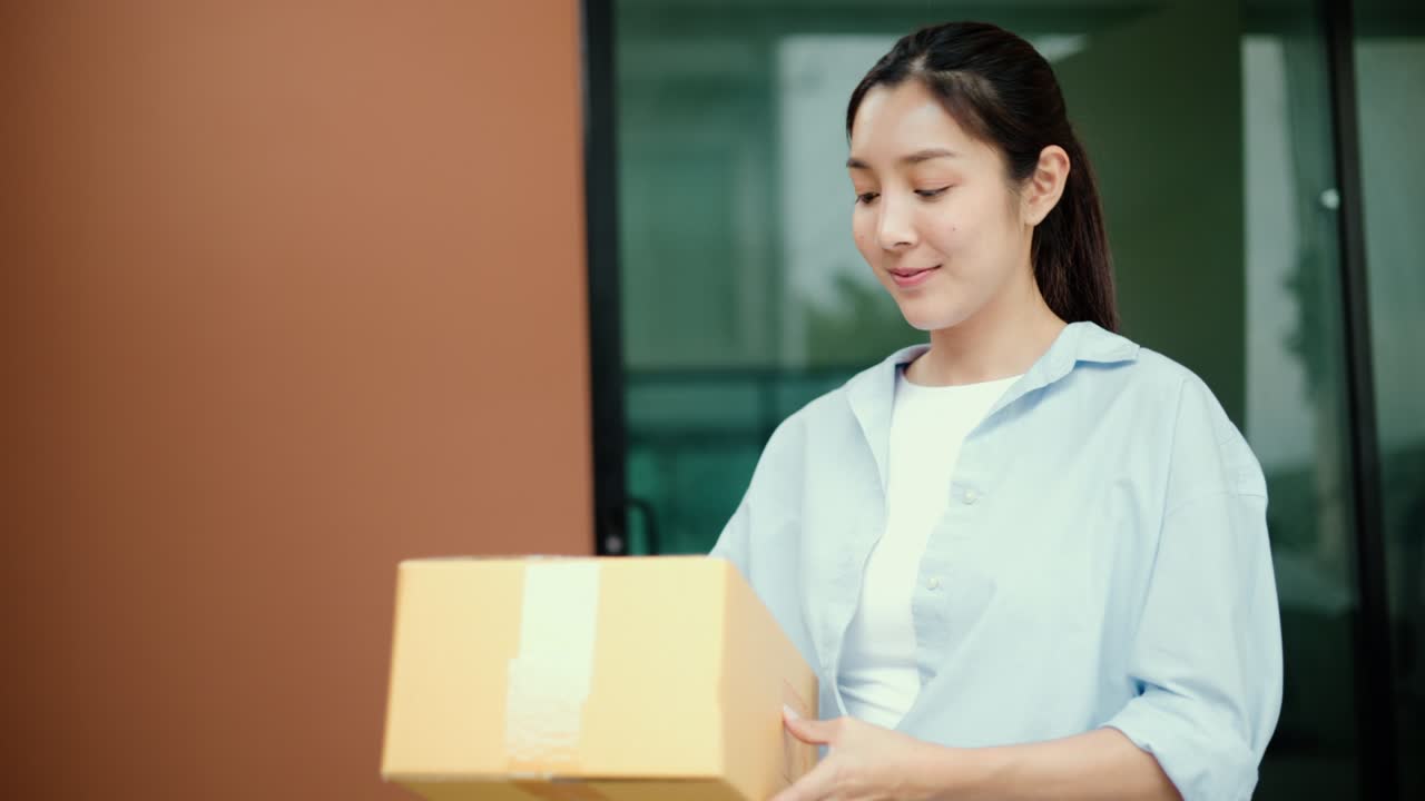 オンラインショッピングで購入した小包を、青い制服の配達員から受け取る若い女性。彼女は契約合意のため、タブレットで電子署名を行っている。配達員は荷物を届け先に配達中である。