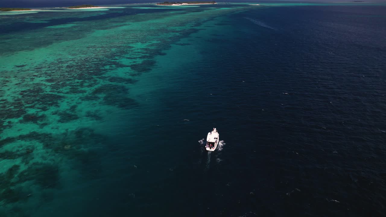 vista aérea de un pequeño bote blanco navegando lentamente en el azul profundo del océano índico en maldivas con una pequeña isla remota en el fondo en un claro día de verano