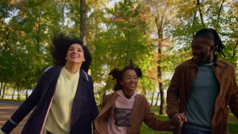 Parents-holding-kid-hands-running-park-walkway-together.-Joyful-autumn-weekend.