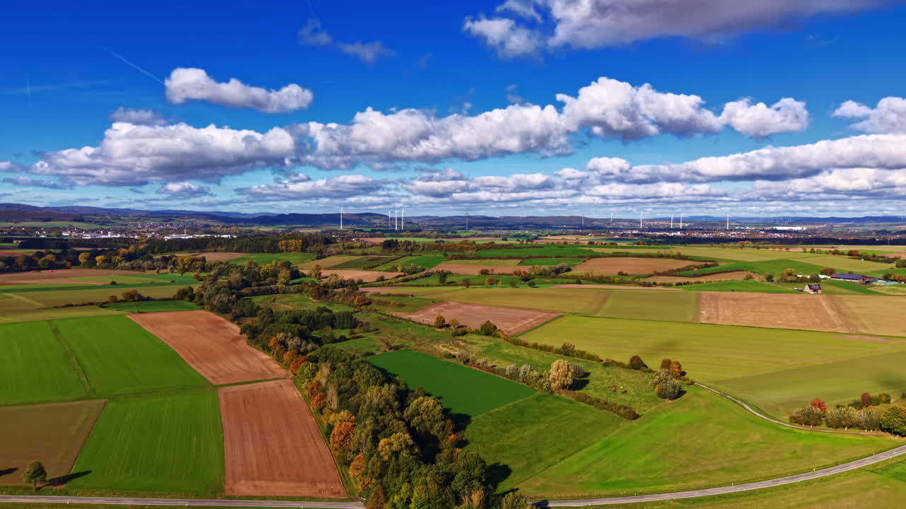 Vibrant landscape of rolling fields under a bright blue sky with fluffy clouds and distant hills during a sunny autumn afternoon