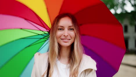 mujer caucásica girando un paraguas multicolor y sonriendo