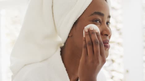 video of happy african american woman in robe cleansing face