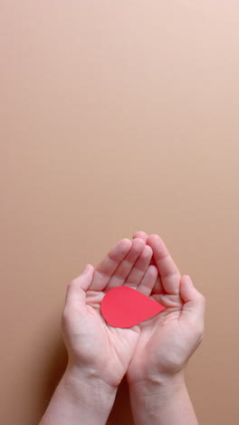 vertical video of hands of caucasian man holding blood drop on beige background with copy space