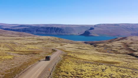 aerial over a black camper van traveling on a dirt road in iceland in the northwest fjords