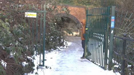 Kaukasischer-Mann-Mit-Orangefarbener-Jacke-öffnet-Ein-Eisernes-Tor,-Das-Den-Besucher-Im-Wald-Des-Weißen-Schneelandschaftsparks-Begrüßt