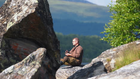 fisherman with casting rod sits on cliff enjoying views at lake ontario in summer