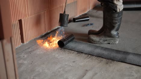 Burning-tar-bitumen-floors-to-waterproof-floor-and-roof,-flaming-sheet-layers-with-propane-gas-burner-blowtorch,-isolation-on-production-site