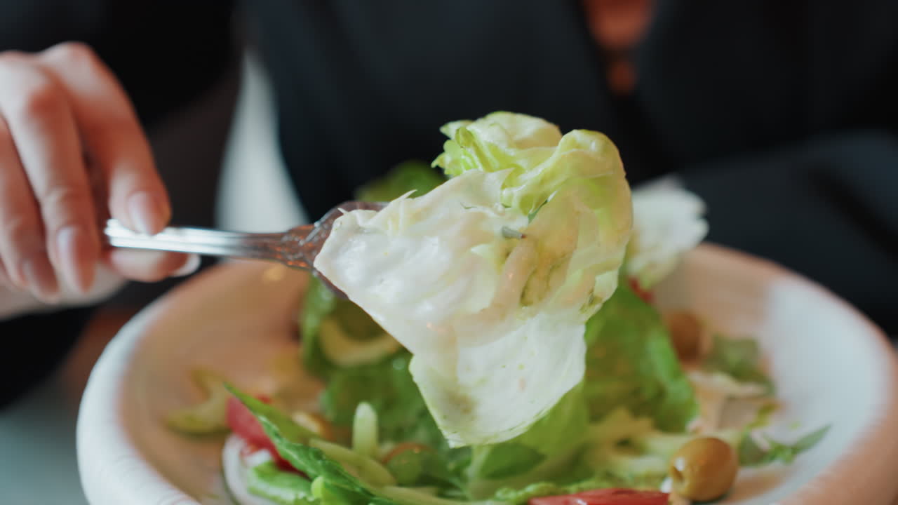 Primo piano di mani che servono un'insalata vivace. Un individuo raccoglie con cura lattuga croccante nella ciotola durante il pranzo. Immagine focalizzata che cattura le mani che preparano un'insalata fresca e salutare in un ambiente da caffè.