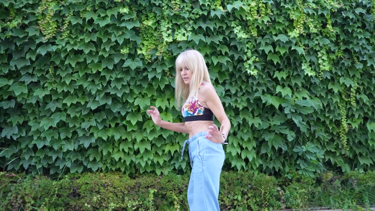 Una donna elegante in abbigliamento sportivo è all'aperto vicino a un muro di edera verde, incarnando uno stile di vita dinamico