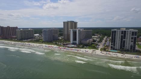 Dolly-shot-of-drone-slowly-descending-above-ocean-looking-towards-ocean-front-resorts