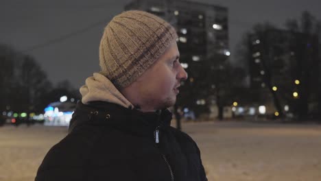 person stand in night city in winter season wearing beanie, close up slow mo