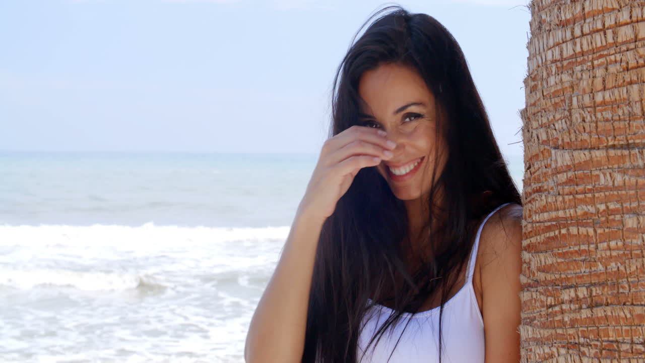 mujer sonriente en la playa apoyada contra un árbol