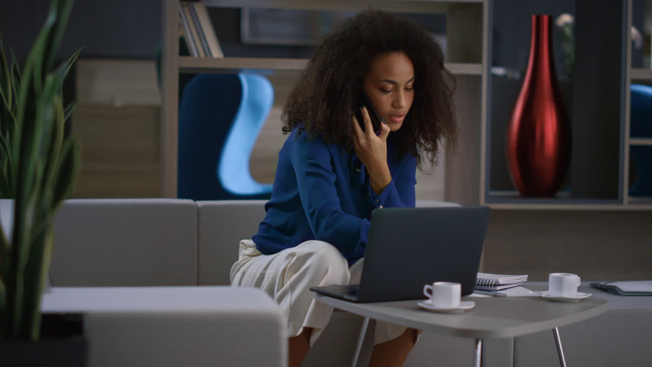 African american business woman writing notes calling phone in home office.
