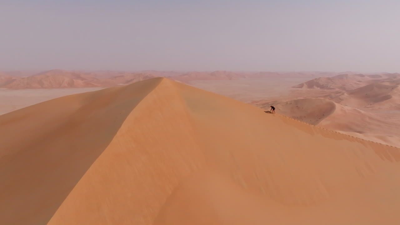 A person walking along the highest dune in Oman’s Empty Quarter desert under the summer sun