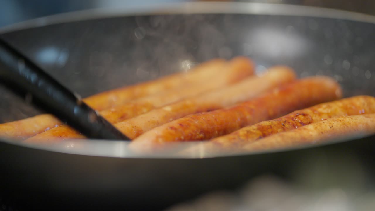 Shallow depth of field shot of tasty sausages cooking and being flipped in a kitchen skillet