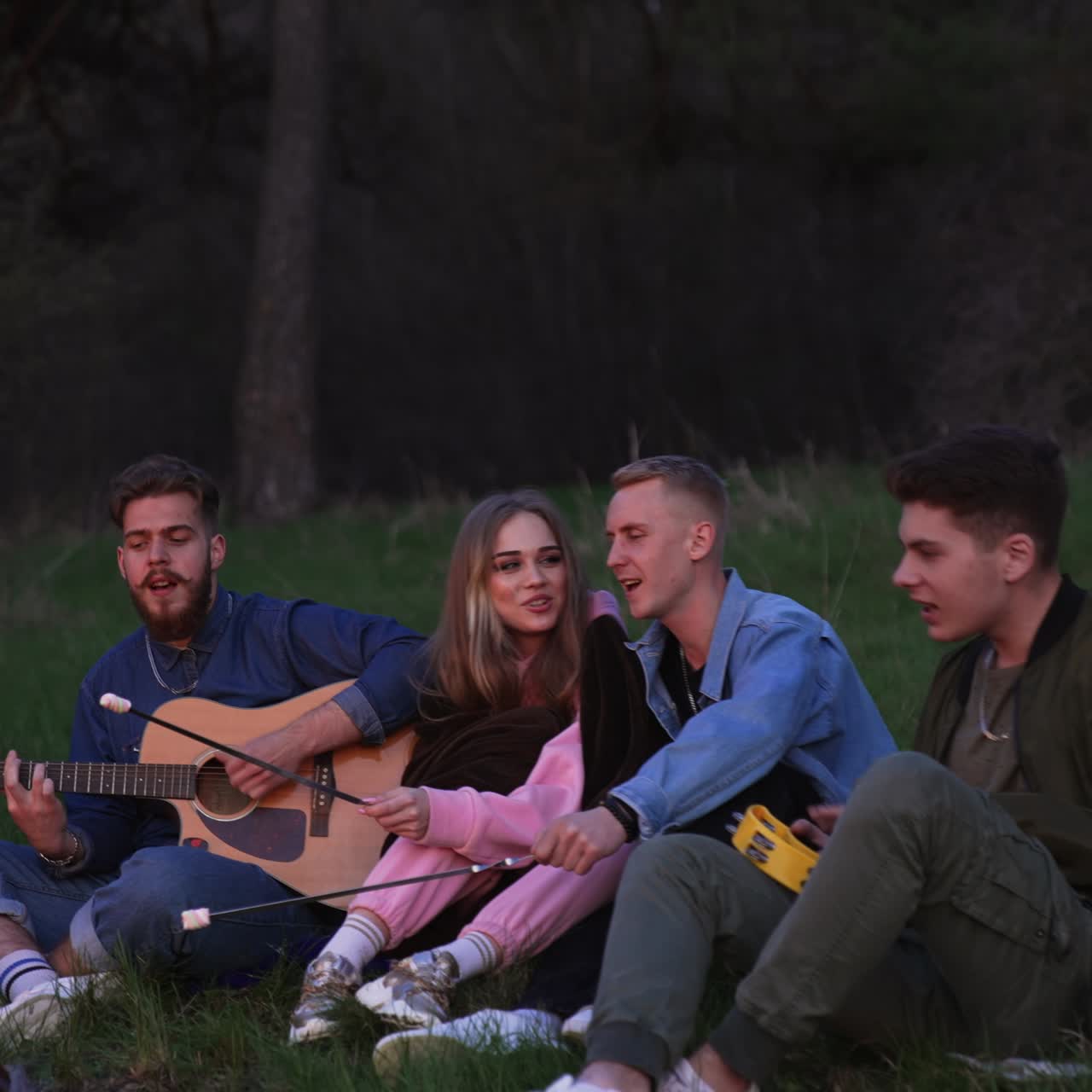 Un gruppo di amici attorno al fuoco suona la chitarra e canta. Amici nella natura seduti attorno al falò