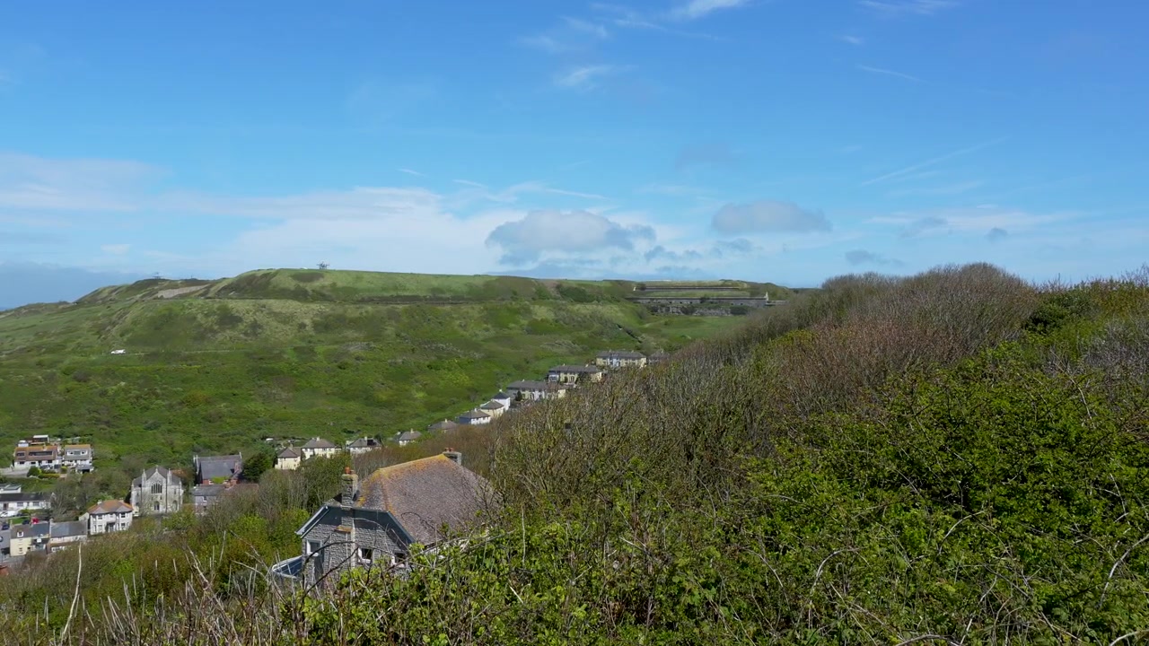 Uma ampla tomada cinematográfica das exuberantes colinas verdes e casas de pedra tradicionais em Weymouth e Portland, Dorset, exibindo a autêntica paisagem rural britânica.