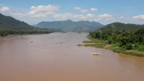 vuelo aéreo sobre el poderoso río mekong en un día soleado con un barco fluvial visto cruzándolo en luang prabang