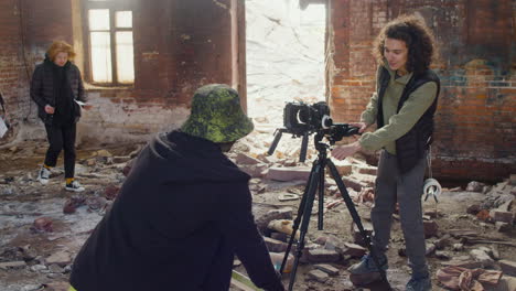 cameraman setting up a camera in a ruined building while another coworker showing a gleaming banner in front of the camera