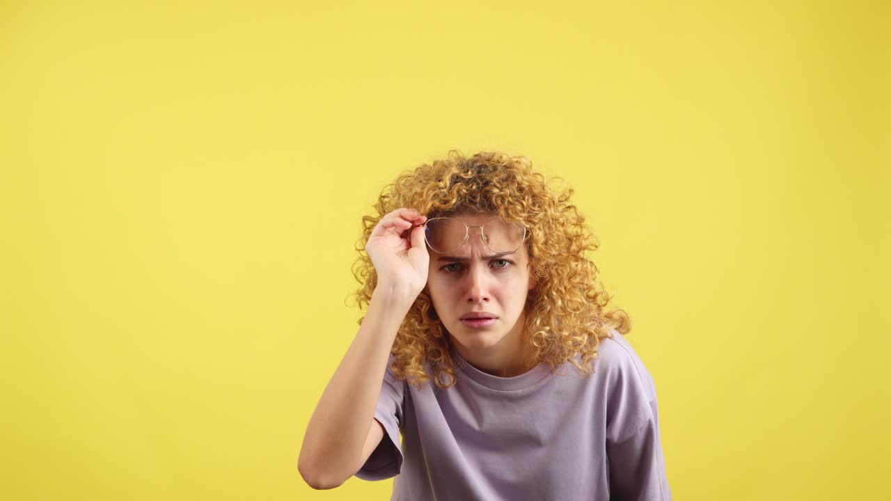 Woman with curly hair and glasses looking intently or struggling to see on a yellow background