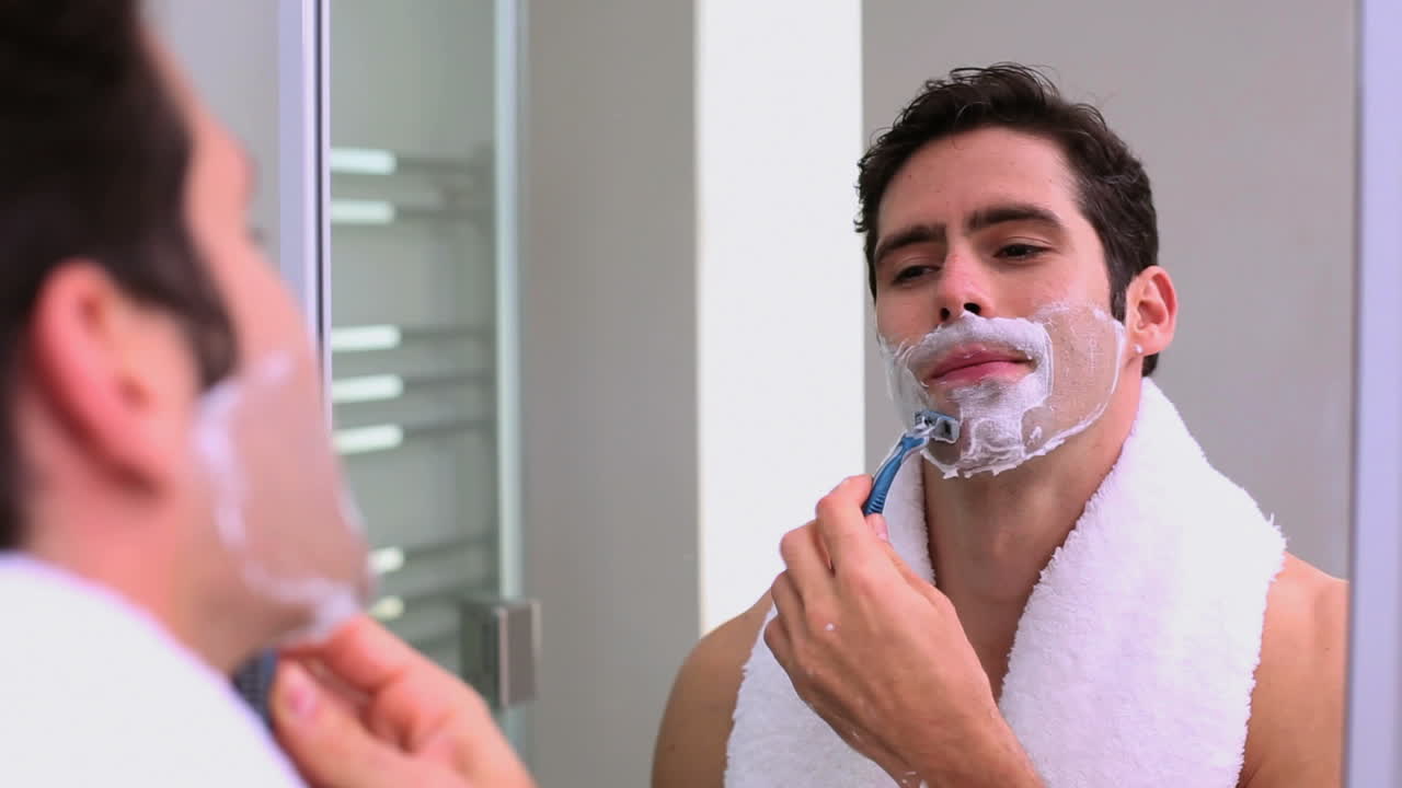 Handsome man looking at mirror and shaving