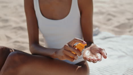 las manos verticales pulverizan aceite de protección solar de cerca. chica atractiva tomando el sol