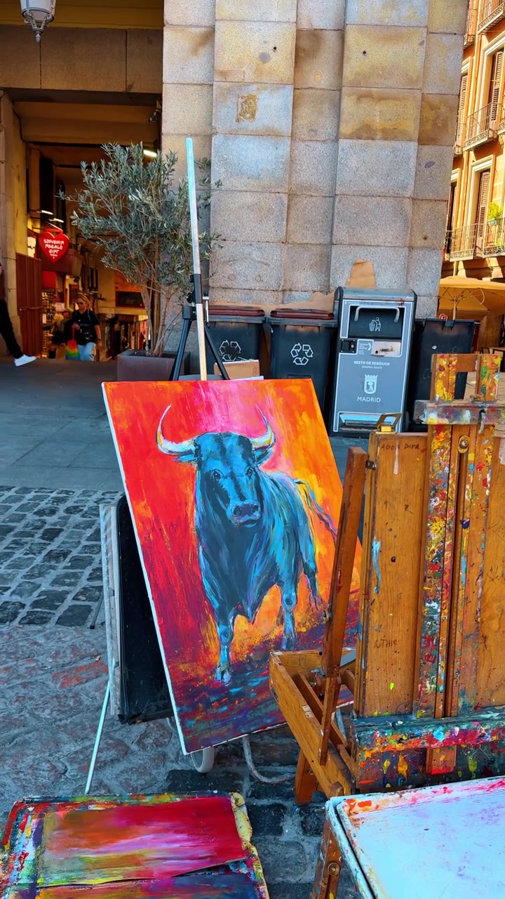 Madrid, España, 8 de agosto de 2025: Caballete de artista callejero con una colorida pintura de toro en la acera de la ciudad. Exposición de arte al aire libre que presenta una vibrante pintura acrílica de un toro en un caballete de madera en una calle urbana.