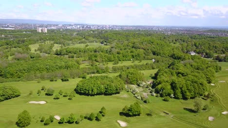 aerial video of a lush golf course surrounded by green fields and trees with a city skyline in the distance