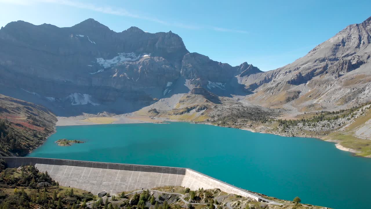 Aerial flyover alongside the hydrolectric dam of Lac de Salanfe in Valais, Switzerland on a sunny autumn day in the Swiss Alps with a view of alpine peaks and cliffs in the distance