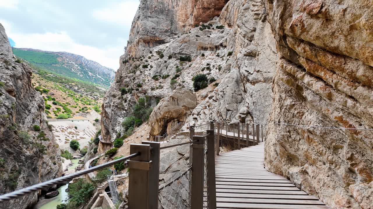 Caminito del Rey'in ahşap yürüyüş yolunda elde çekilmiş POV (bakış açısı) yürüyüş çekimi, büyüleyici kireçtaşı kayalıklarını ve kanyon derinliğini ortaya çıkarmak için hızlı bir 180 derecelik sola kaydırma içeriyor