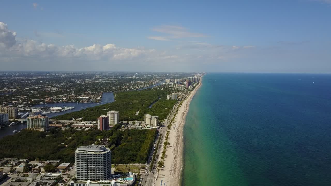 Aerial view of a vibrant coastal city with high-rise buildings, a long sandy beach, and clear blue ocean waters stretching to the horizon under a bright sky.