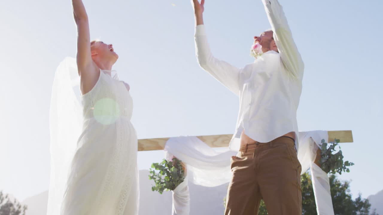 행복 한 백인 신혼 부부, 야외 의 제단 앞 에 꽃잎 을 던지는 점프