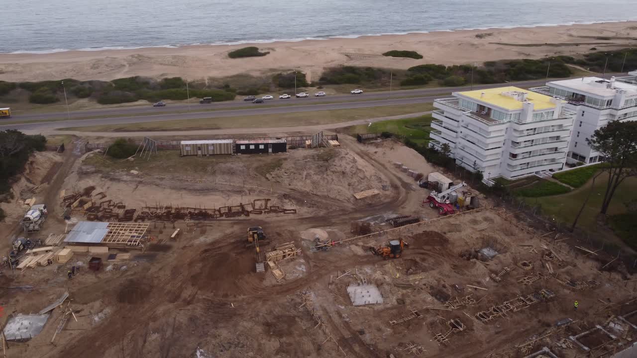 vista aérea del sitio de construcción frente al océano y la playa de arena de punta del este - camiones en la carretera costera conduciendo a lo largo