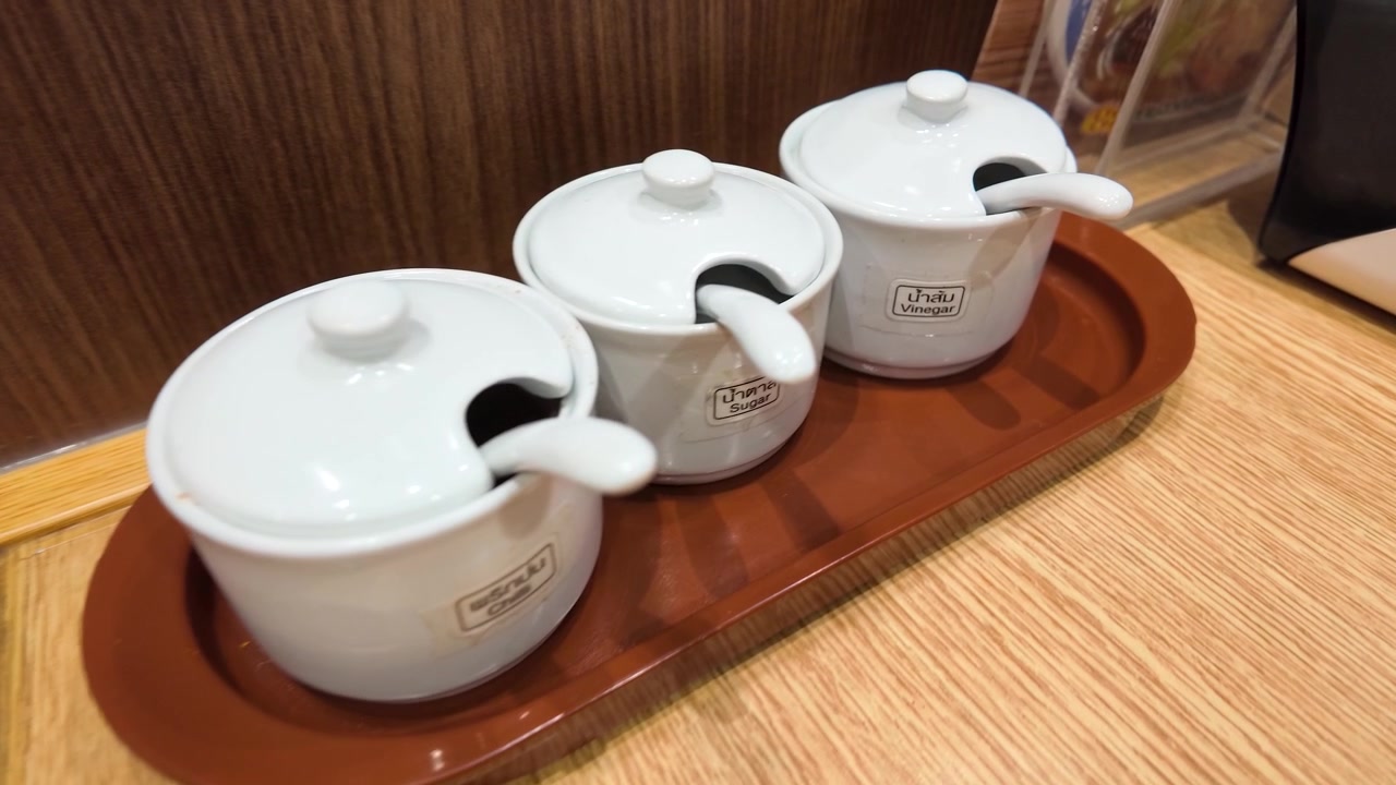 Close-up zoom of white ceramic condiment jars on a wooden tray in a restaurant.