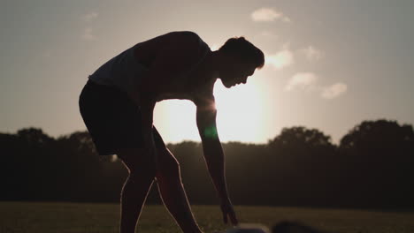 man stretching his legs before a run whilst being silhouetted by the evening sun in slow motion