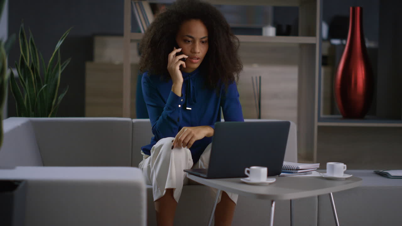Afrikansk-amerikansk forretningskvinde diskuterer finansiel rapport via mobiltelefon på kontoret.