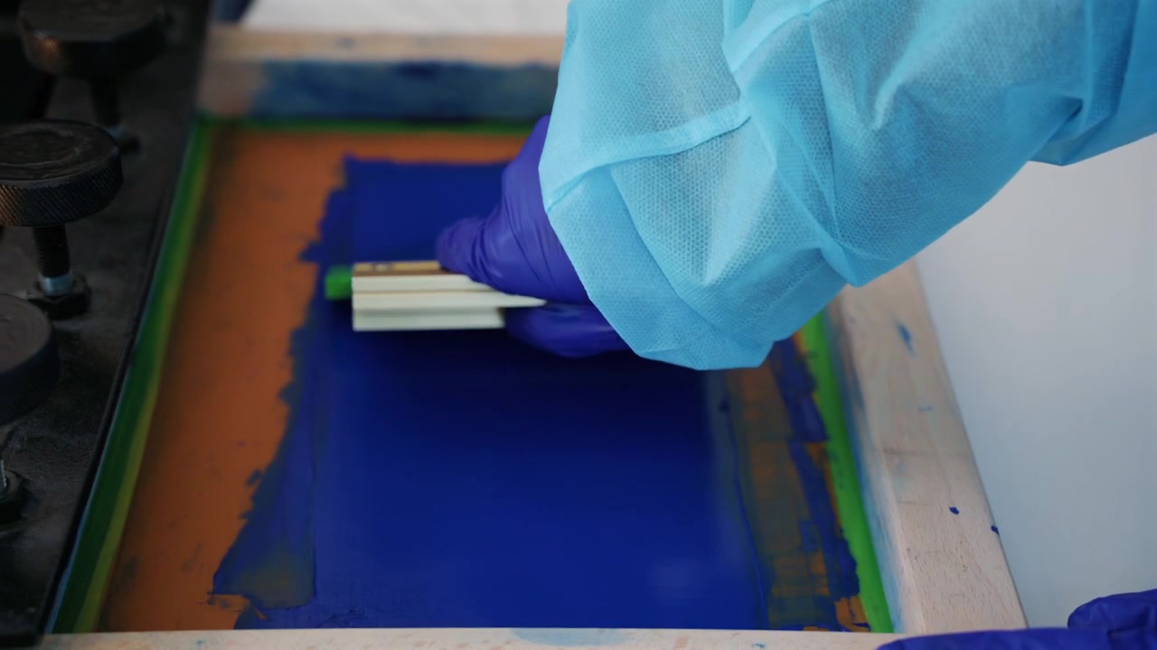 Worker using a squeegee to spread ink across a screen printing frame during textile production
