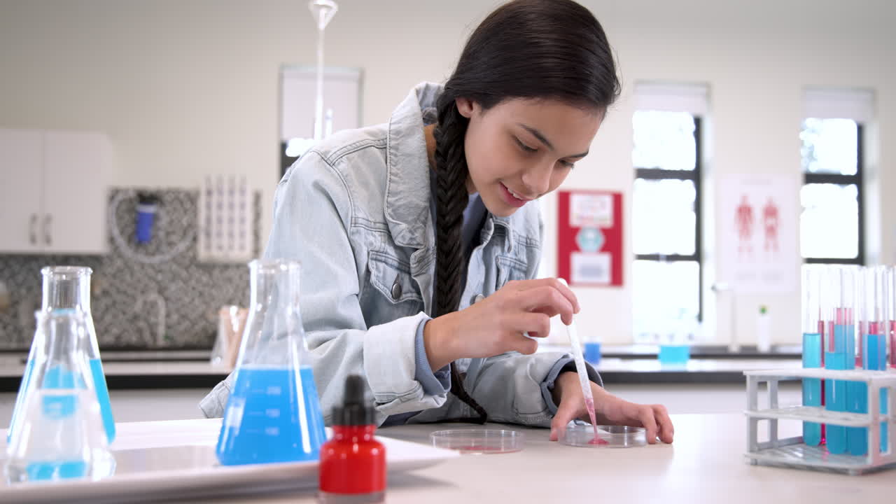 Girl in science class using pipette with petri dish, focused on experiment, at school