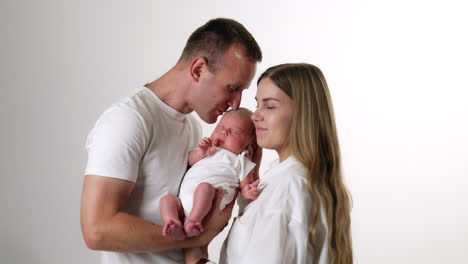 happy smiling man holding his newborn baby. loving mom leans to her beloved child. white backdrop.