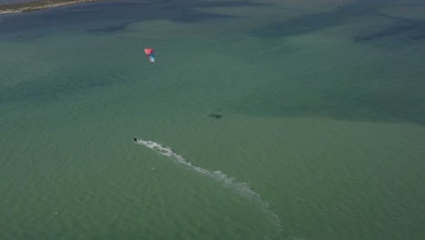 Siguiendo-De-Cerca-Y-Luego-Volando-Sobre-Kitesurf-En-Aguas-Verdes-Del-Océano,-Antena-De-Drones,-Fuzeta