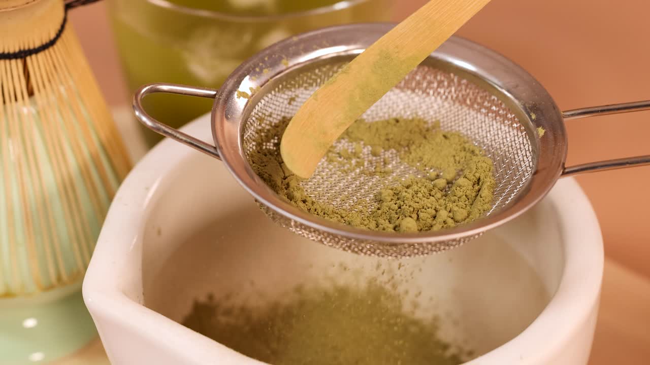 Matcha powder sifted through fine mesh strainer into bowl, warm lighting, close-up, steady camera
