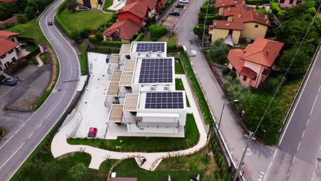 drone shot of compact white housing block with rooftop solar grid, surrounded by mediterranean homes and intersecting streets. riva di solto, italy riva di solto, italia