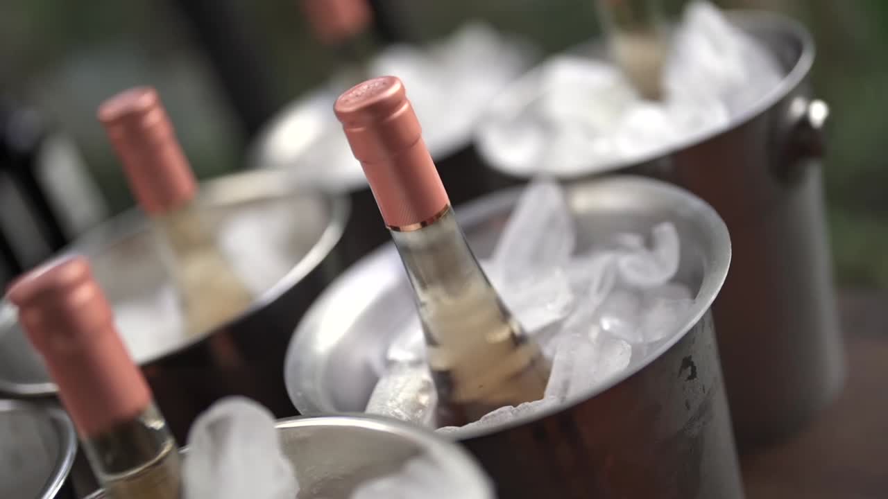Several champagne white sparkling wine bottles with rose-gold caps nestled in polished stainless steel buckets filled with crystal-clear ice