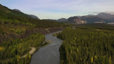 Aerial-flyover-following-Sag-river-stream-surrounded-with-forests-and-high-mountains-in-Deadhorse,-Alaska