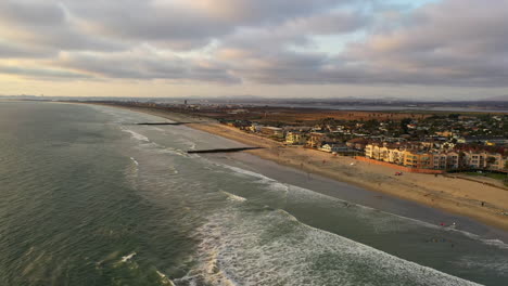 Foamy-Waves-Running-Ashore-With-Jetties-And-Beachfront-Buildings