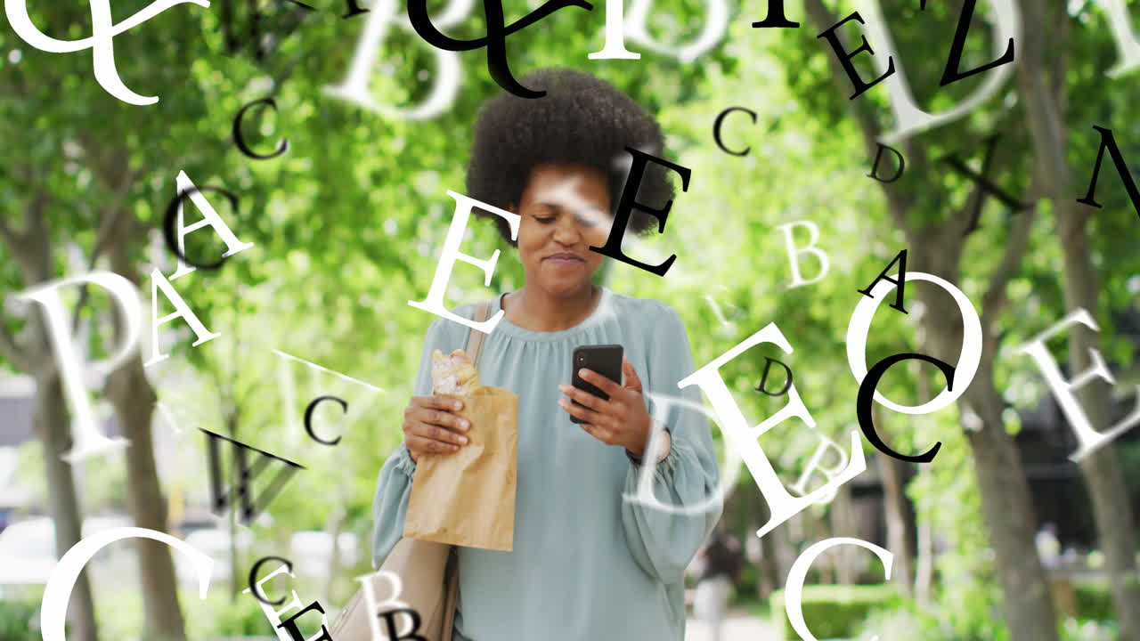 Animation of letters, african american woman walking and scrolling on cellphone while eating hotdog