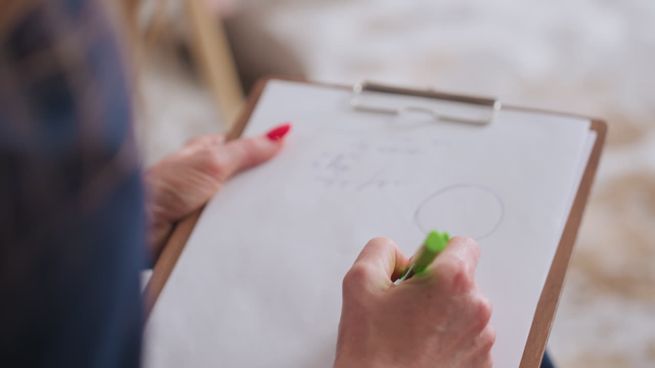 Close view of guide drawing on notebook during session with client, focus on hand and pen movement, soft lighting and blurred background create calm setting for therapeutic communication