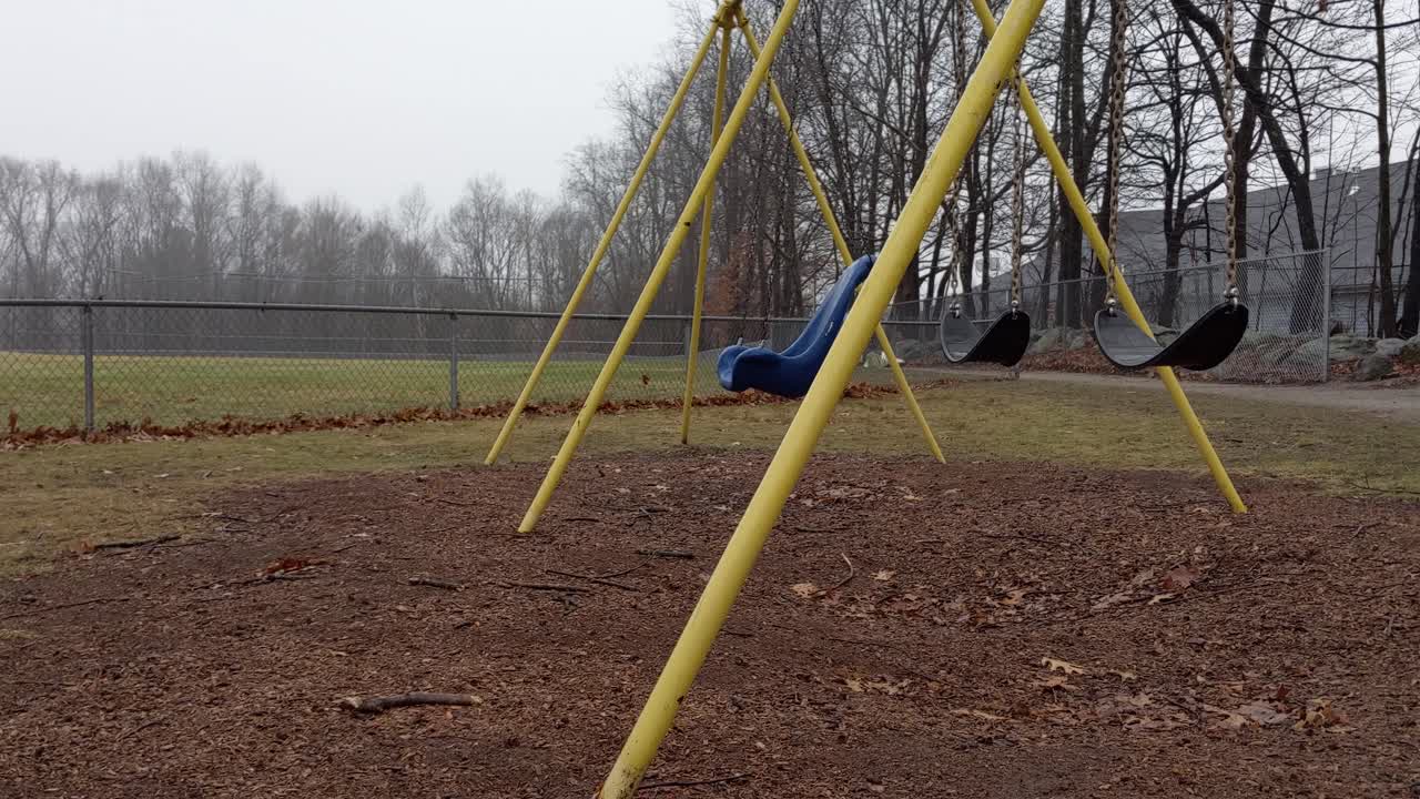 Deserted playground swings swinging empty and lonely on a rainy and dreary day
